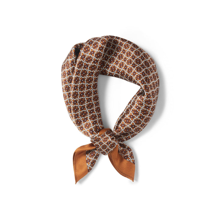 The Lucky Clover Square Silk Scarf from SusanSilk, featuring a repeating white and dark brown pattern, tied in a simple knot.