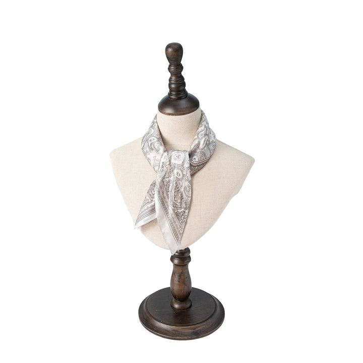 A mannequin bust on a wooden stand is adorned with a SusanSilk Paisley Series Square Silk Scarf tied around the neck.