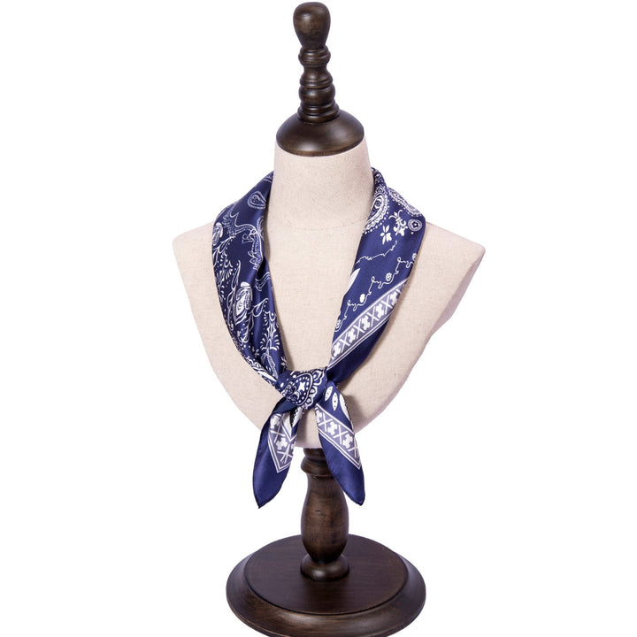 A navy and white Paisley Square Silk Scarf by SusanSilk is tied around the neck of a dress form mannequin on a dark wooden stand.