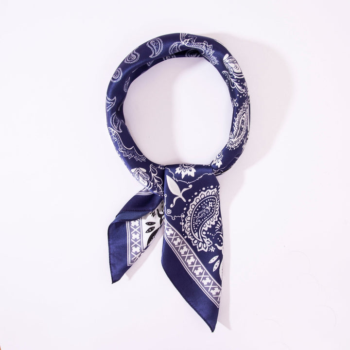 A neatly folded Paisley Square Silk Scarf in navy and white, arranged in a circular shape with one end tucked under, showcasing a hint of SusanSilk elegance.