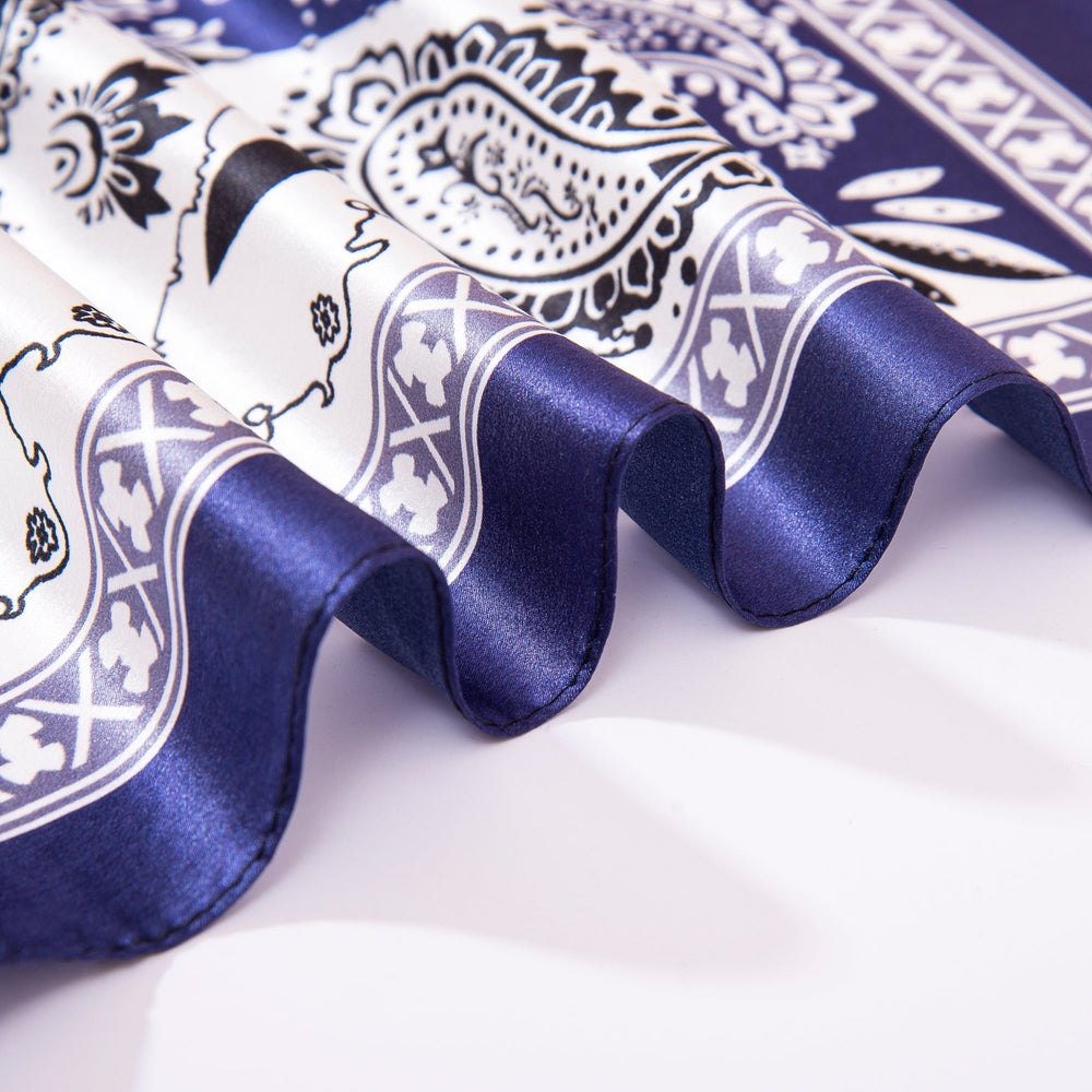 Close-up of a folded SusanSilk Paisley Square Silk Scarf in Navy/White. The scarf features a blue and white paisley pattern, and has a smooth, shiny texture.