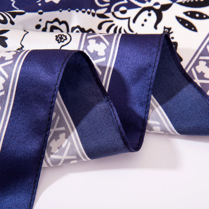 Close-up image of a folded Paisley Square Silk Scarf - Navy/White by SusanSilk, showcasing white and navy blue floral and geometric designs. The silk fabric boasts a smooth, shiny texture.