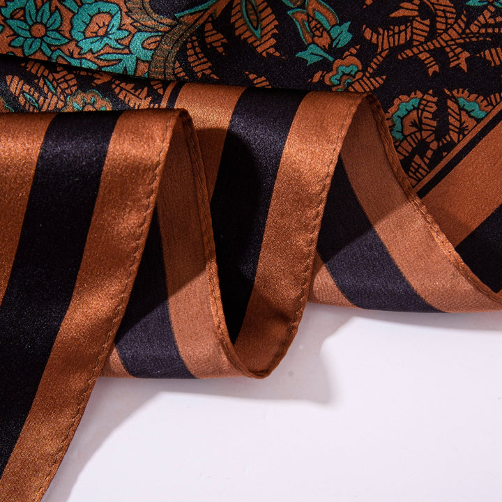 Close-up of a Paisley Square Silk Scarf - Retro from SusanSilk, showcasing alternating brown and black stripes with a floral pattern accented by green. The fabric appears draped and smooth in texture.