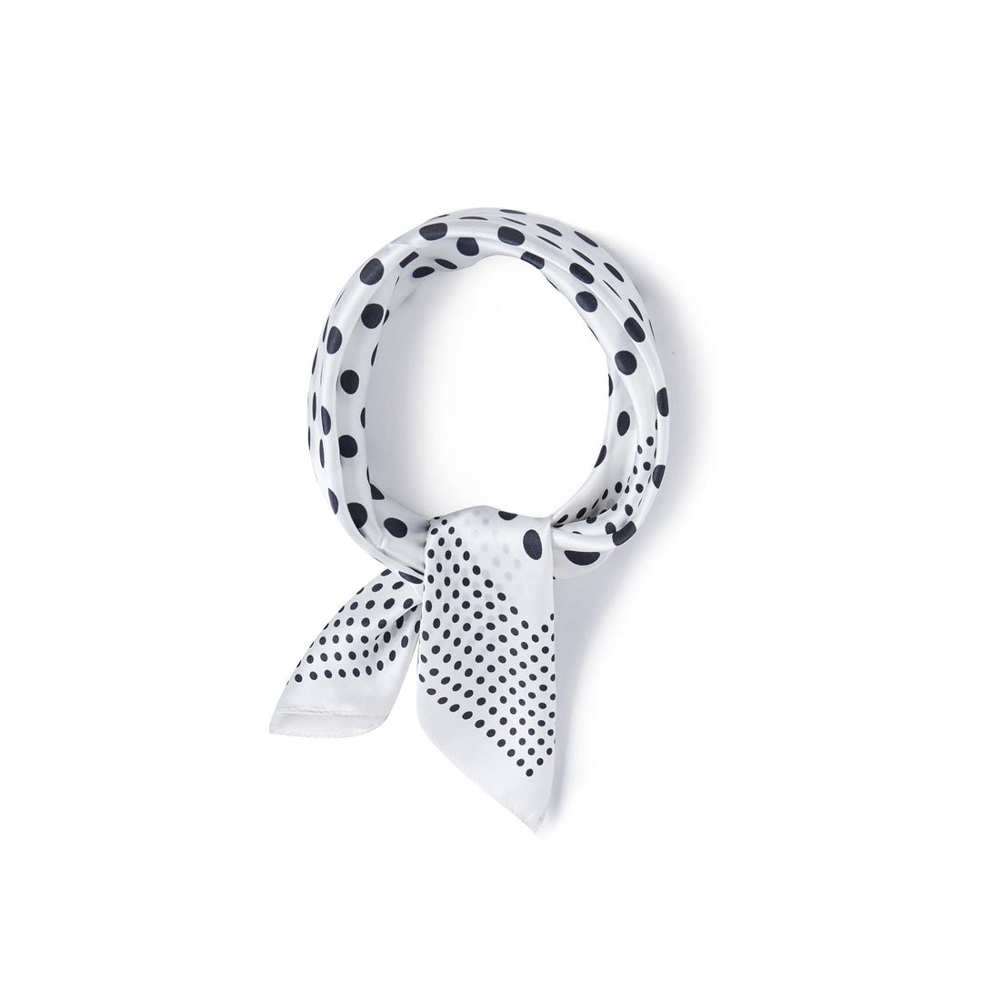 A SusanSilk Polka Dot Square Silk Scarf, featuring black polka dots on a white background, is tied into a loop with a small knot at the bottom.