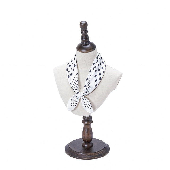 A white mannequin wearing the SusanSilk Polka Dot Square Silk Scarf, tied in front, displayed on a wooden stand.