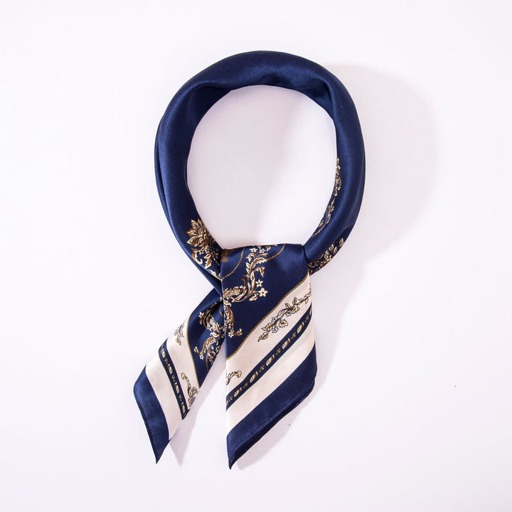 A Royal Pattern Square Silk Scarf by SusanSilk, in navy blue and white with a decorative design, is neatly folded in a circular shape against a plain white background.