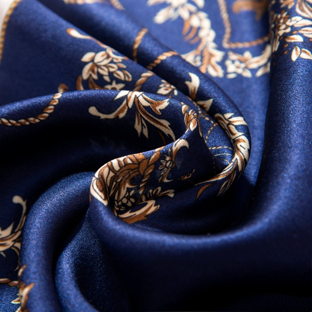 Close-up of the Royal Pattern Square Silk Scarf by SusanSilk, showcasing its twisted, blue fabric with a gold floral pattern.